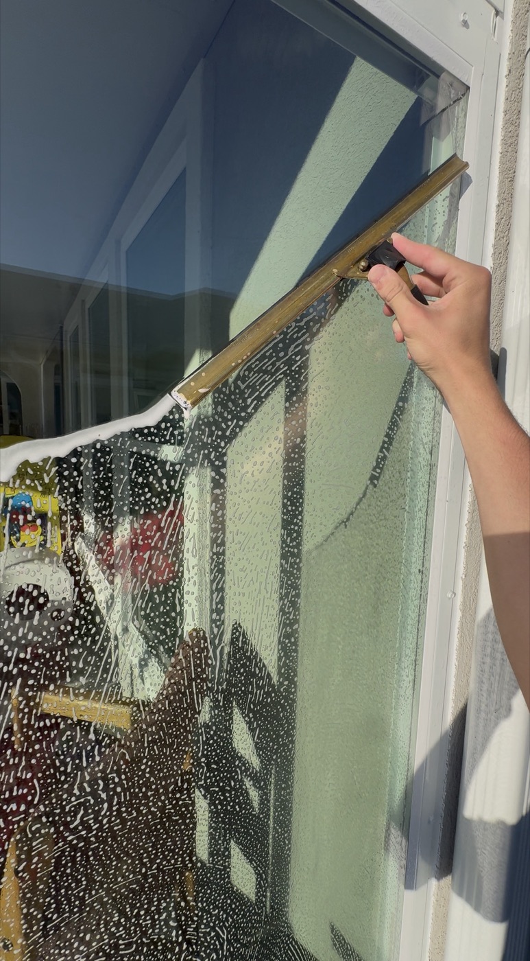 Brass professional squeegee pulling soapy water off a window, mop and squeegee method